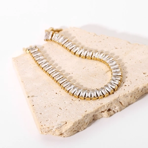 Dettaglio del bracciale dorato con zirconi taglio baguette su pietra di travertino