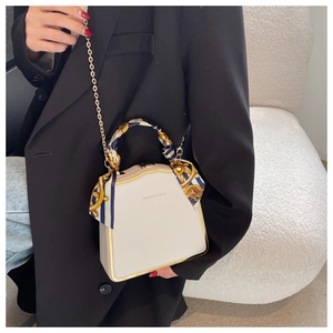 Detail of cream box bag with gold metal frame, printed silk scarf handle and chain strap