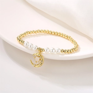 Detalle de pulsera de cuentas doradas con colgante de luna creciente, circón y perlas