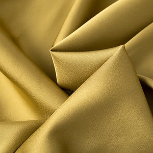 Macro detail of glossy golden satin fabric with elegant silk texture and soft spiral folds