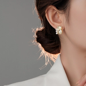 Detail view of gold square stud earrings with three pearls on a model ear