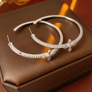Detailed view of silver hoop earrings with zircon cross charms on a jewelry box