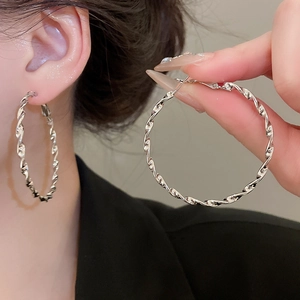 Detailed view of silver twisted geometric hoop earrings worn by a model