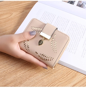 Detail of beige faux leather wallet featuring laser-cut leaf pattern and gold pendant