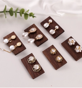 Detail view of pearl earrings on vintage walnut wood display stand with green leaf accents
