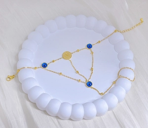 Detail of gold evil eye hand chain bracelet with relief coin charm on a white tray