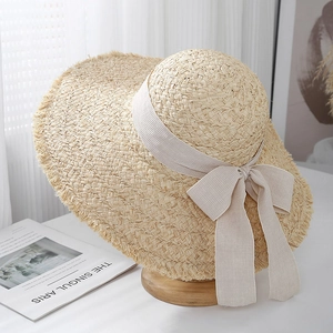 Detail of hand-woven raffia sun hat featuring an elegant beige bow and frayed edge trim