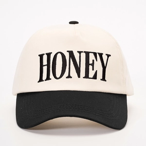 Detail shot of 'HONEY' embroidery on a two-tone beige and black baseball cap