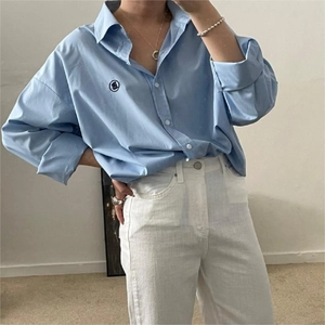 Detail of a simple silver necklace worn with a light blue oversized cotton shirt