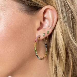 Close-up of model wearing rainbow hoop, emerald chain stud, and silver ear cuff