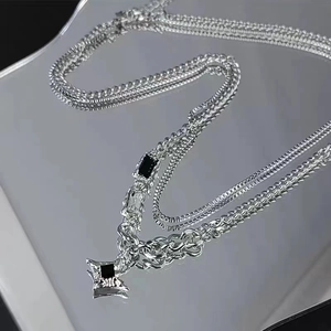 Detail of silver layered necklace with black star pendant reflected on dark mirror surface