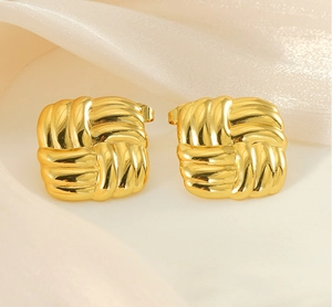 Close-up of golden square stud earrings with woven texture on soft beige silk