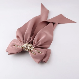 Close-up of pink satin bow hair clip with luxury rhinestone center and long ribbons