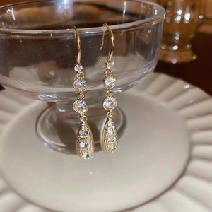 Close-up of elegant gold tassel earrings hanging on glass with cubic zirconia details