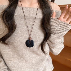Collier vintage avec pendentif rond en bois et résine noire sur un pull beige élégant