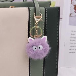 Plush purple soot sprite bag charm with big eyes and gold clasp on a handbag