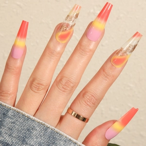 Long coffin gradient press-on nails with pink orange yellow hues and gold glitter accents