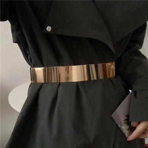 Polished gold metal mirror cinch belt styled over a black trench coat for women