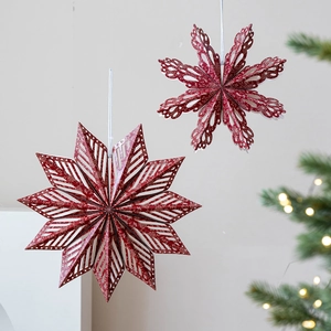 Red Nordic paper snowflake and star ornaments hanging with festive Christmas tree background
