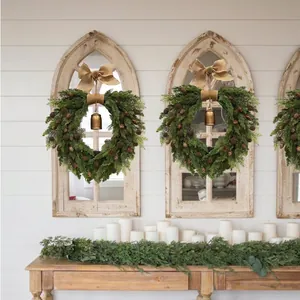 Christmas wreath with burlap bow, pine cones, and bell hanging on an arched mirror