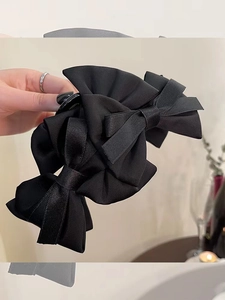 Detailed close-up of a large black satin bow hair claw clip with an elegant layered design