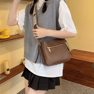 Brown rectangular shoulder bag with pattern strap and gold zipper details in cafe setting