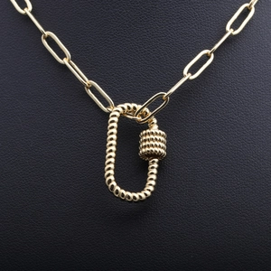 Collier chaîne trombone dorée avec pendentif mousqueton texturé sur fond noir chic