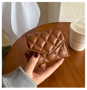 Close-up of a brown quilted leather clutch bag held over a cafe table setting