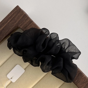Detail of a delicate black pleated mesh hair scrunchie on a wooden display tray