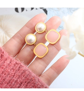 Close-up of gold-plated drop earrings with white pearls and square pink stone pendants
