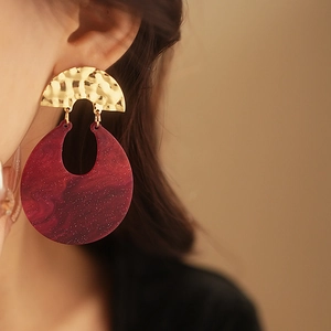 Macro detail of red resin drop earring with gold hammered texture on female model