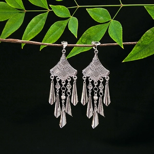 Ethnic style silver tassel drop earrings hanging on a natural branch with green leaves