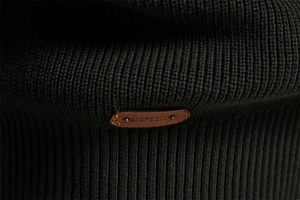 Detail of dark green ribbed knit fabric featuring premium brown leather brand patch