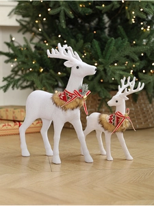 Detail of two white flocked Christmas reindeer with red bows and bells in a cozy setting