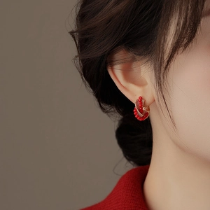 Close-up of model wearing twisted golden hoop earrings with red crystal beads