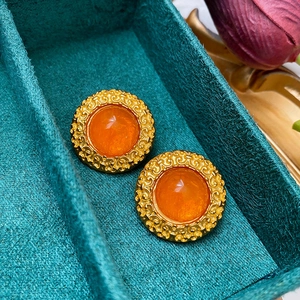 Detailed close-up of vintage golden round earrings with orange resin in a velvet box