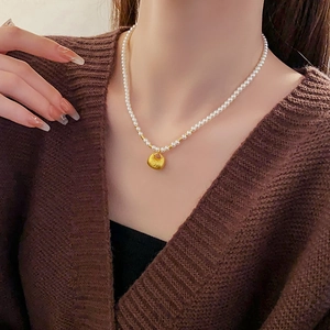 Close-up of pearl necklace with a gold oval lucky charm pendant on a model