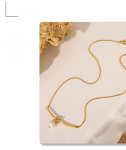 Detail of a minimalist gold necklace with a white pearl and curved tube pendant