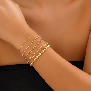 Close-up of five-piece gold layered bracelet set with mixed chain designs on wrist