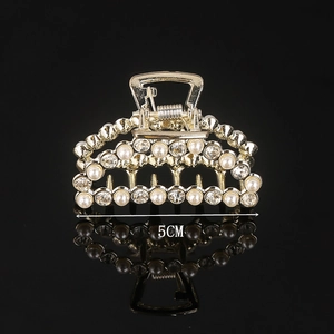 Detail of 5cm golden alloy hair claw with pearls and rhinestones on black background