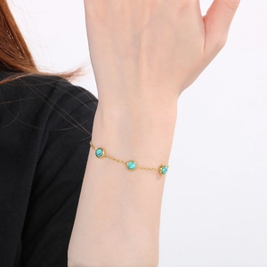 Détail d'un bracelet en chaîne dorée avec trois pierres turquoise bleues au poignet