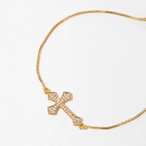 Macro shot of gold cross bracelet with shimmering stones and delicate chain link details