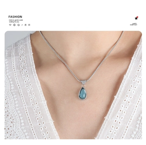 Close-up of blue teardrop crystal pendant on silver snake chain worn by female model