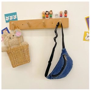 Close-up of blue denim kids chest bag hanging on hook with decorative bear and accessories