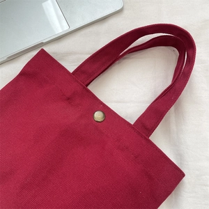 Close-up of the burgundy canvas tote bag featuring a vintage metal snap button detail