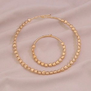Dettaglio del set di collana e bracciale a cuore in oro lucido su raso beige morbido