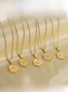 Detail of 18K gold stainless steel hexagonal initial pendants on yellow silk background