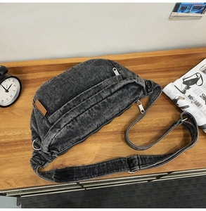 Detailed flat lay of a dark gray washed denim chest bag with adjustable strap on wooden table