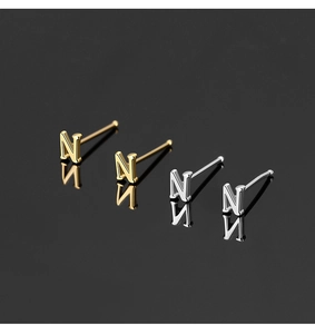 Detailed view of silver and gold letter N nose studs on a reflective black background