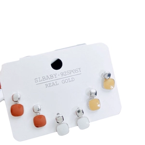 Three pairs of geometric square stud earrings in brick orange, pearl white, and lemon yellow